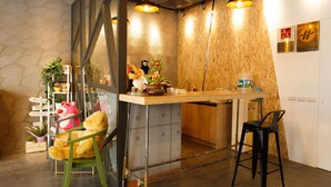 A reception area with a wooden counter, a green chair, and a black chair. There are signs on the wall and a plant on the left. - PS Hotel (Jiaoxi)