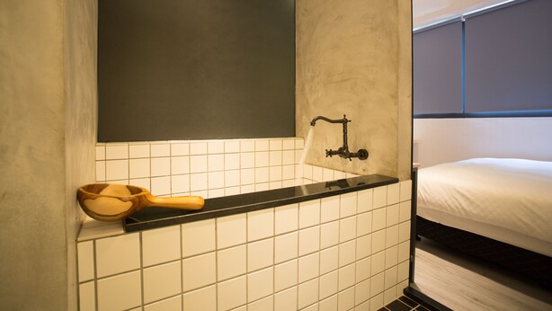 A bathroom with a black countertop, a wooden basin, and a white tiled wall. - PS Hotel (Jiaoxi)