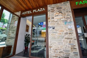 De ingang van Hotel Plaza met een stenen gevel, een houten plafond en een glazen deur.
