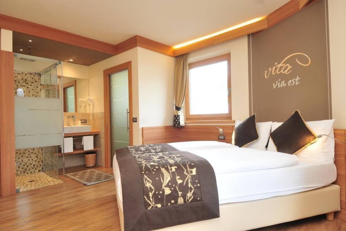 A hotel room with a large bed, a bathroom with a mirror, and a window.