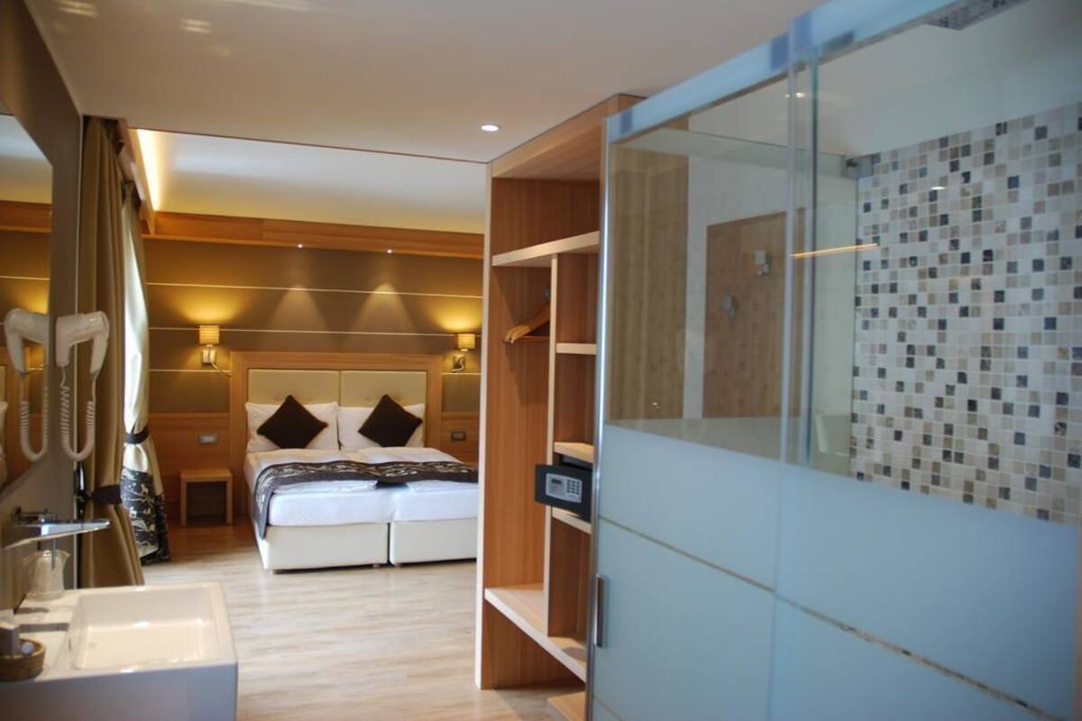 A modern hotel room with a large bed, a walk-in closet, and a glass shower enclosure.