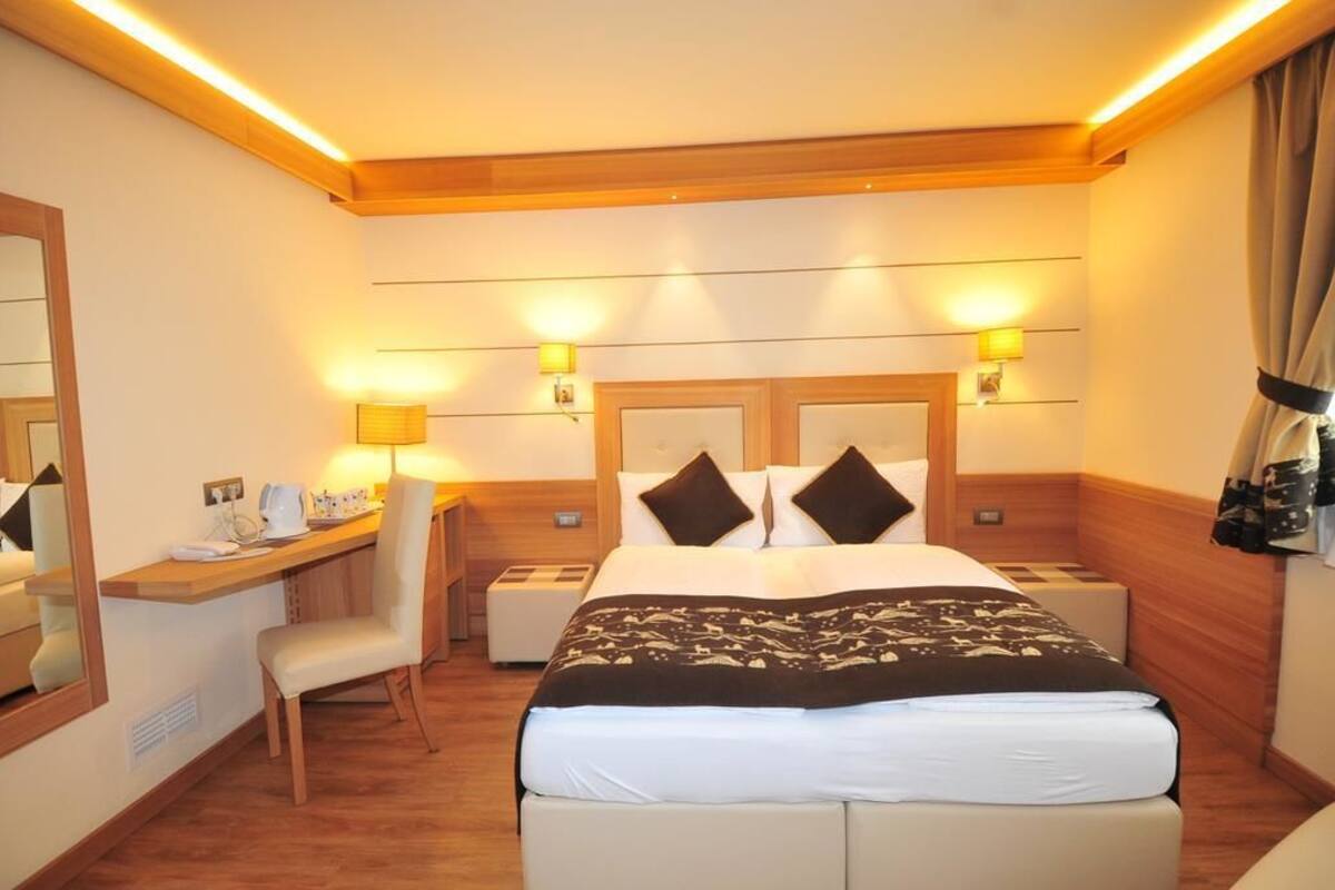 A hotel room with a bed, bedside tables, a desk with a chair, and a mirror.