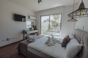 Habitación de hotel moderna con cama, escritorio, televisor de pantalla plana y balcón con vistas a palmeras.