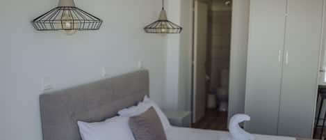 A neatly made bed with white linens, a grey headboard, and a swan-shaped towel. There are two pendant lights above the bed, and a wardrobe is visible in the background.