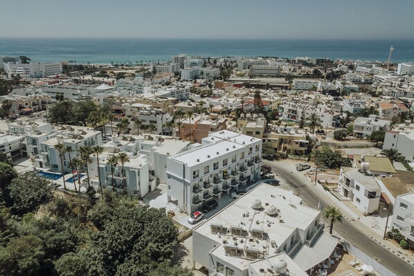 An aerial view of a coastal urban area with modern buildings, a clear sky, and the ocean in the background.