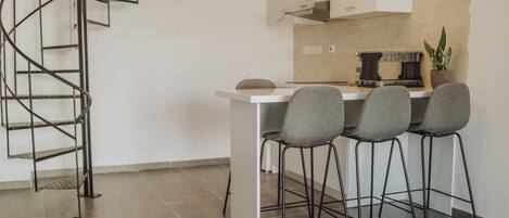 Une cuisine moderne avec un plan de travail blanc, quatre chaises grises, un escalier en colimaçon noir en métal et une plante en pot posée sur le plan de travail.