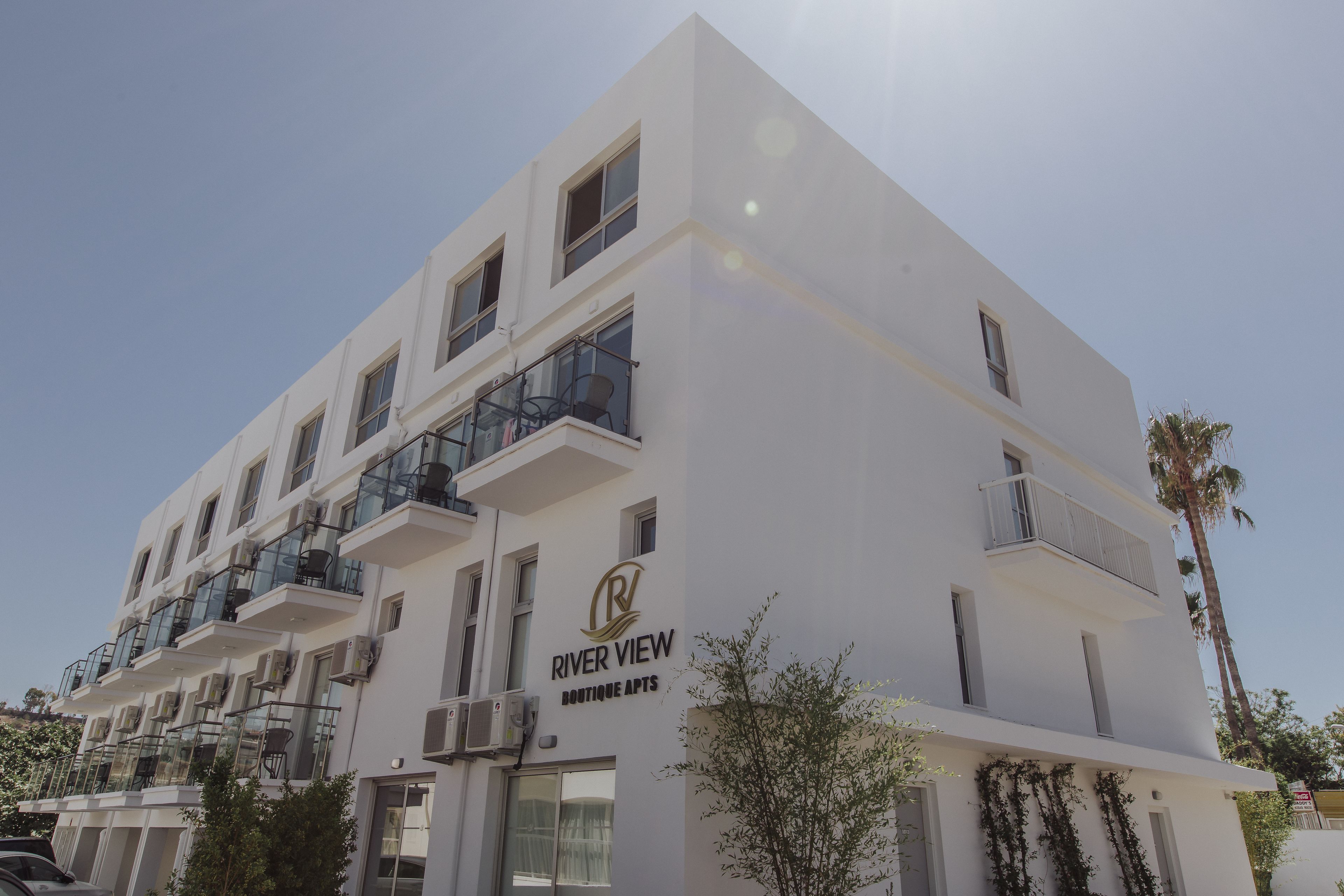 A multi-story building with balconies, air conditioning units, and a sign reading "RIVER VIEW BOUTIQUE APARTS".