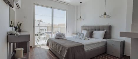A modern bedroom with a large bed, bedside tables, a desk with a telephone, and a sliding glass door leading to an outdoor area.