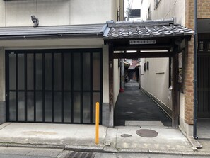 A narrow alleyway with a traditional tiled roof entrance, a metal gate, and a yellow pole.