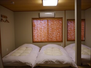 A room with two beds, an air conditioner, and a window with blinds.