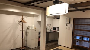 A compact kitchen with a microwave, refrigerator, and sink. There's a dining table with a black tablecloth and a wooden cutting board. - Kyoto Machiya UZUKI (Kyoto)