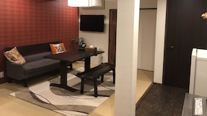 A living room with a sofa, coffee table, and bench. There is a TV mounted on the wall and a door to the right. - Kyoto Machiya UZUKI (Kyoto)