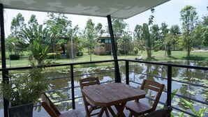 A covered outdoor seating area with a table and chairs, overlooking a pond with lily pads and greenery. - The Lampang Villa (Lampang)