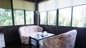 A room with wooden flooring, a table with floral chairs, a window with a view of greenery, and a small appliance on the left. - The Lampang Villa (Lampang)