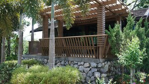 A wooden gazebo with a stone base, surrounded by lush greenery and trees. - The Lampang Villa (Lampang)