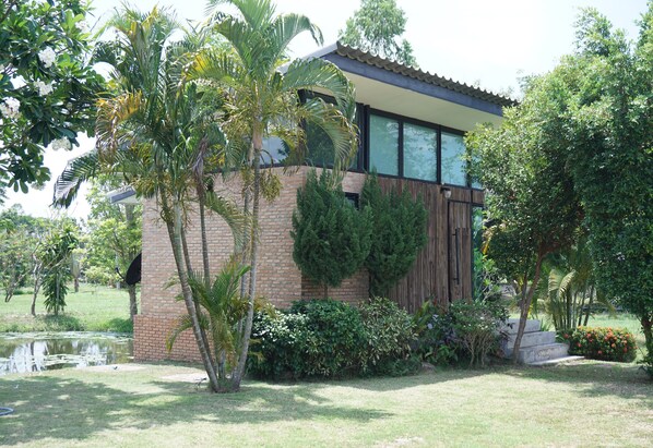 A modern house with a brick exterior, large windows, and a well-maintained garden with various plants and a small pond. - The Lampang Villa (Lampang)