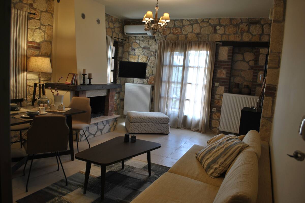 A living room with a stone wall, a fireplace, a sofa, a coffee table, and a television mounted on the wall.