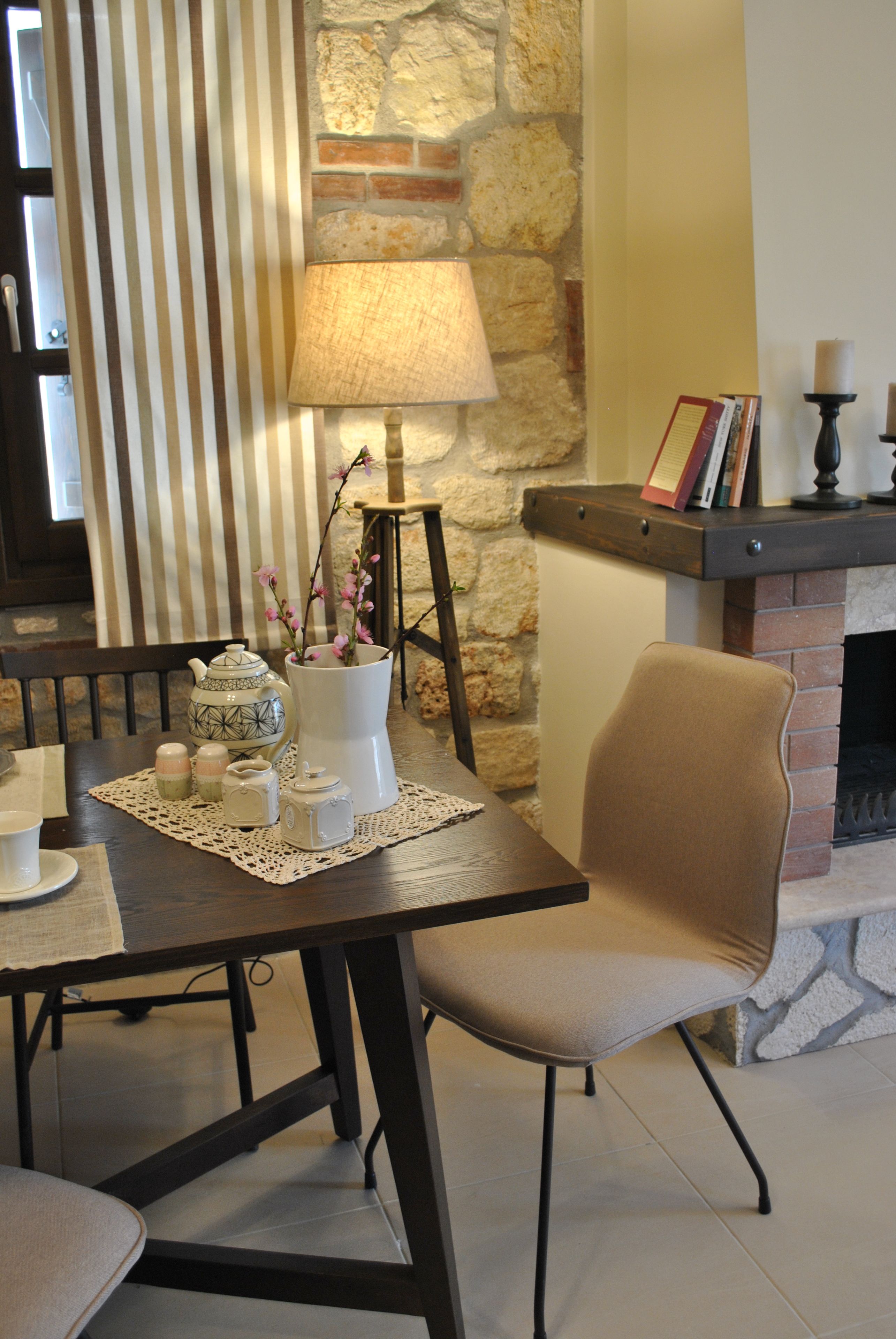 A dining area with a table set for two, a chair, a lamp, and a fireplace.
