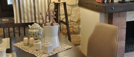 A dining area with a table set for two, a chair, a lamp, and a fireplace.
