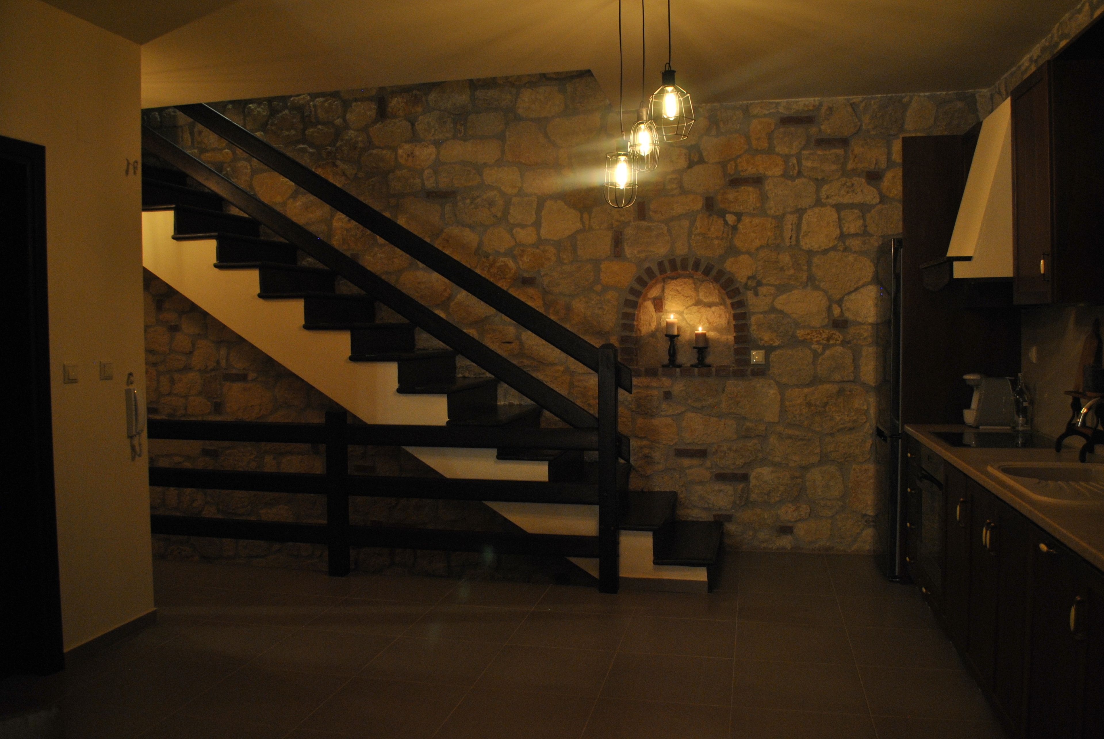 Escadaria com parede de pedra, área de cozinha com armários escuros e luminária pendente.