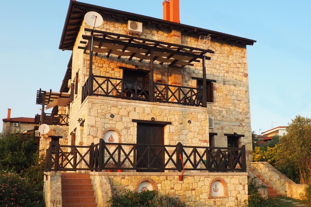 A two-story stone building with a balcony, a small door, and a chimney.
