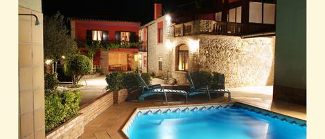 A swimming pool with lounge chairs, a stone wall, and a red building in the background.