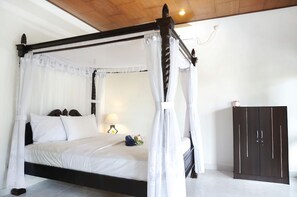 A four-poster bed with white linens and a canopy, a bedside table with a lamp, and a dark wardrobe. - Bungalow No 7 (Lembongan Island)