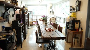 A spacious kitchen with a long wooden table, various kitchen appliances, and a large window providing natural light. - Hostel Foryou (Yeosu)