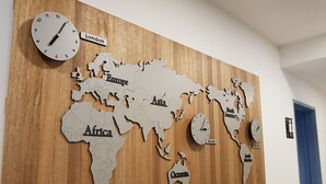 A wooden wall with a world map and clocks indicating different cities. - Hostel Foryou (Yeosu)
