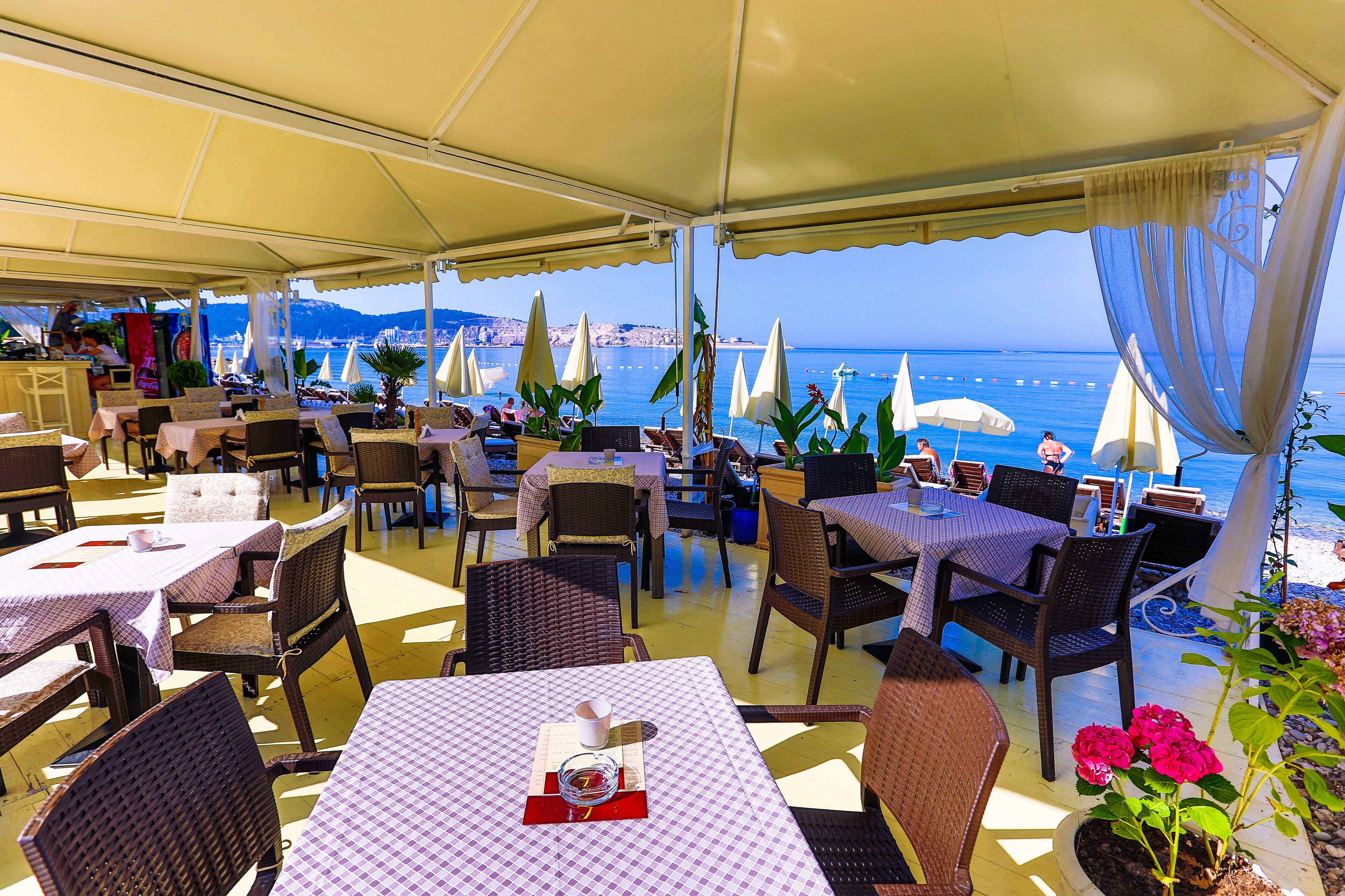 An outdoor dining area with tables and chairs, umbrellas, and a view of the sea.