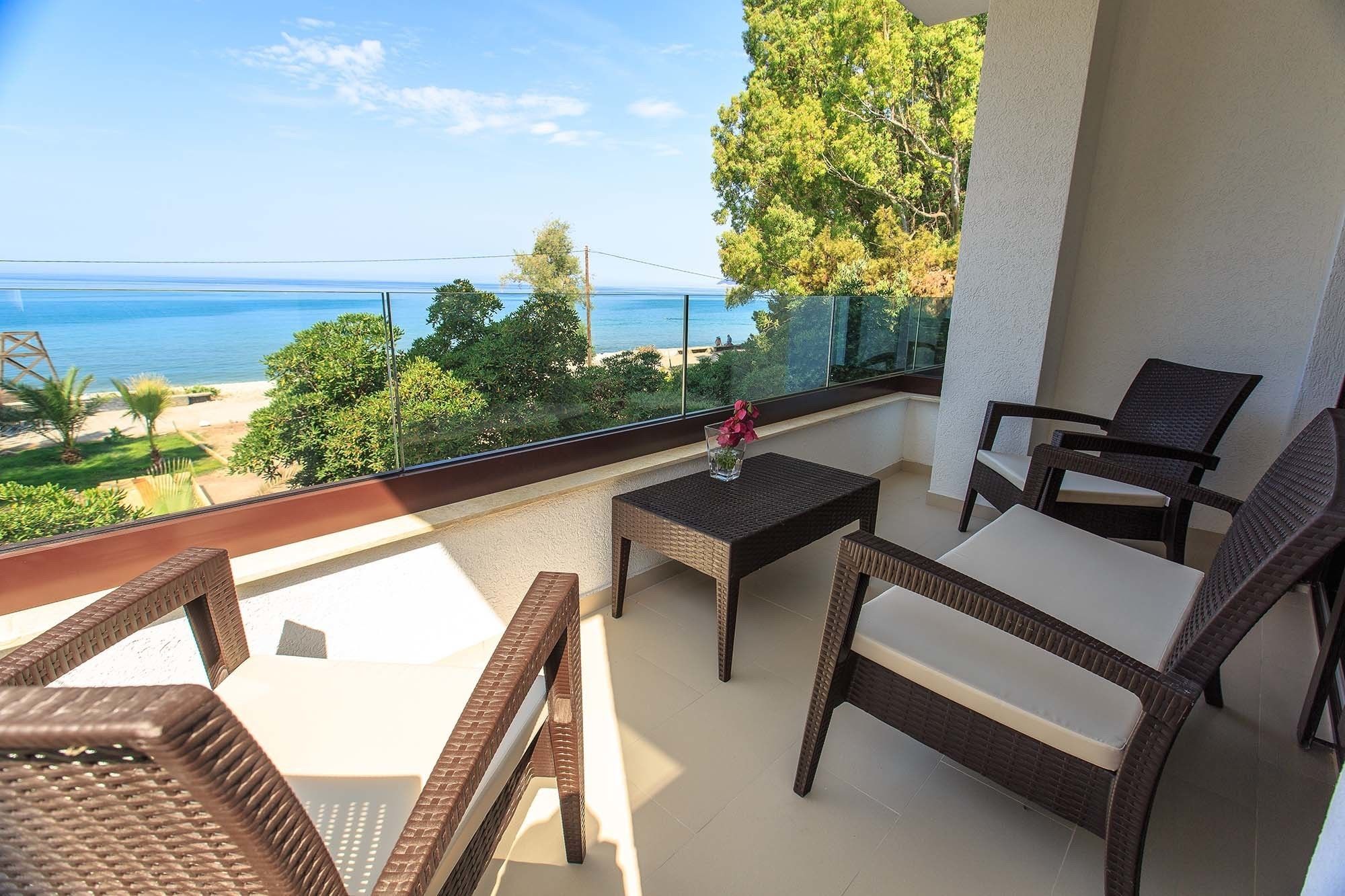 Un balcón con mobiliario de mimbre, una mesa de vidrio y vistas al mar y al follaje.