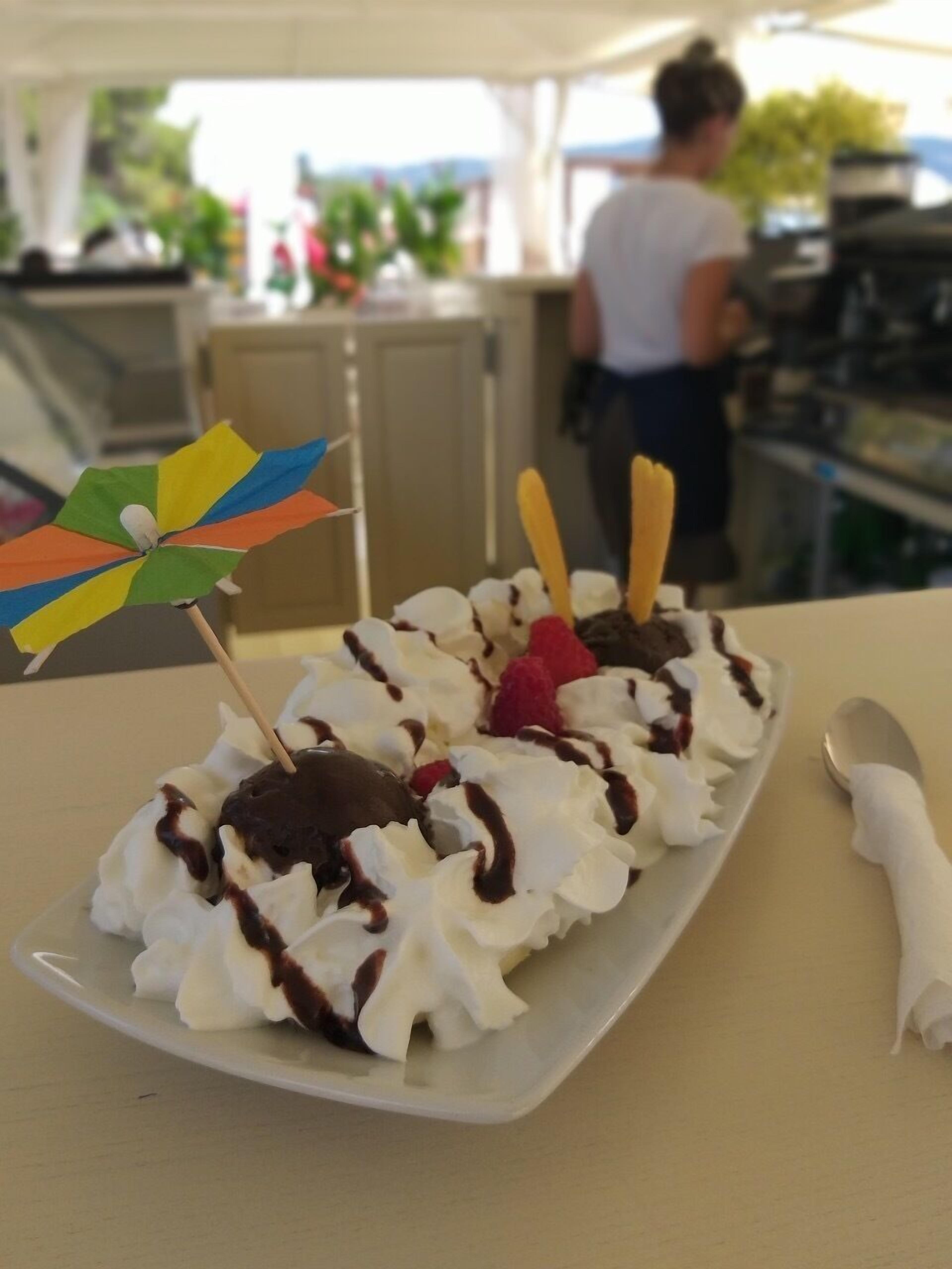 Un plato de postre con crema batida, chocolate y fruta sobre un plato blanco.