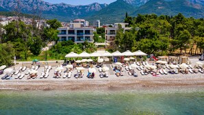 A beachside hotel with sun loungers and umbrellas, a pool, and a view of mountains in the background. - Apartments Kuce Lekovica snack bar- Bistro & Beach  (Bar)
