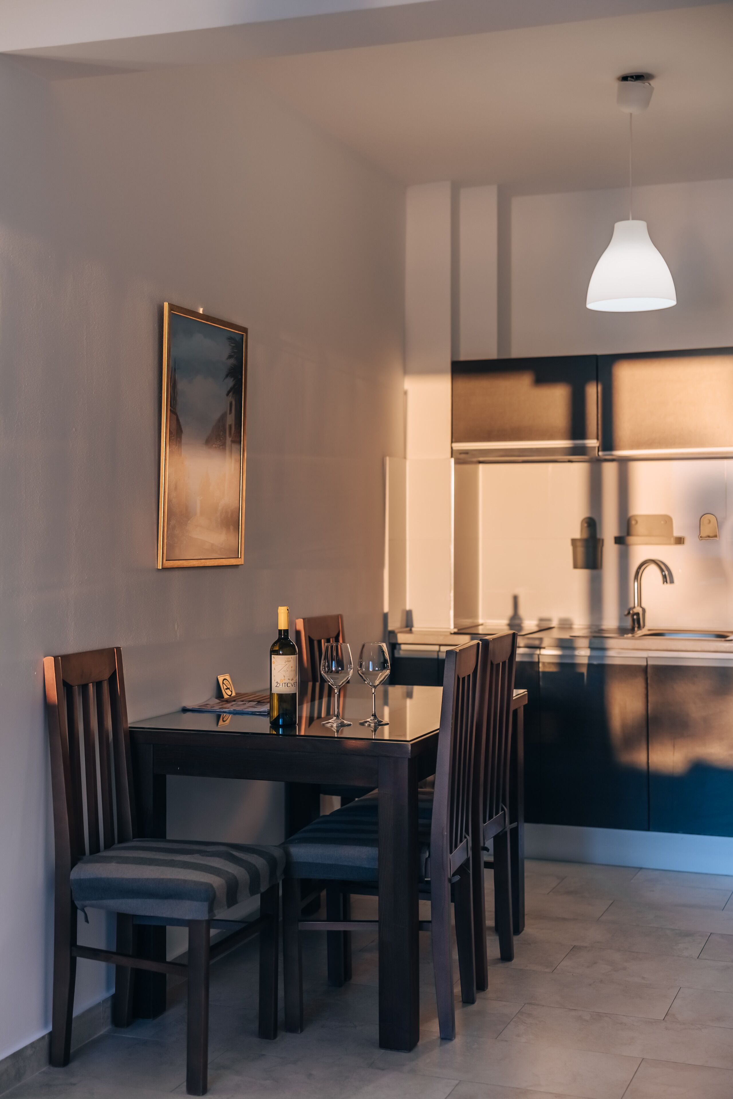 Un comedor con una mesa dispuesta para seis personas, una botella de vino y copas. Hay un cuadro en la pared y una lámpara colgante sobre la mesa.