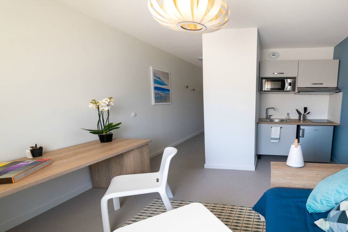 En kompakt opholdsstue med tekøkken, spiseplads og siddeområde med sofa og stol.