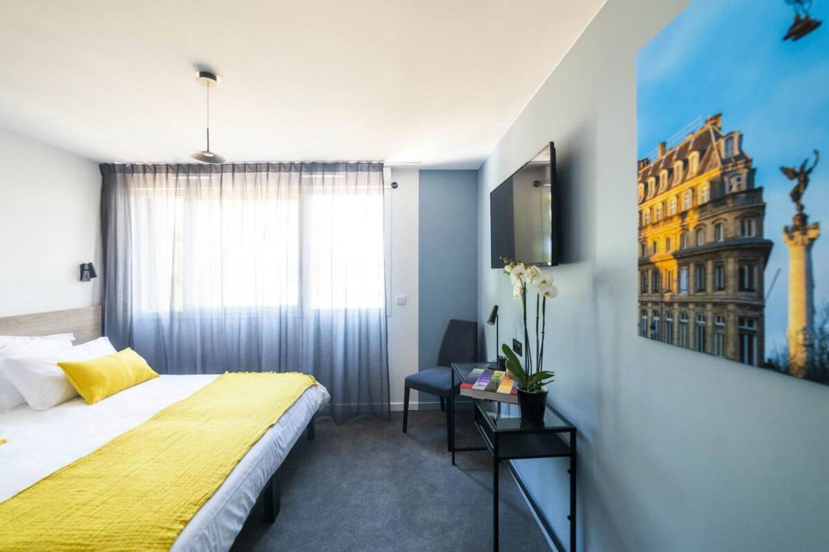 Et hotelværelse med seng, skrivebord, stol, fjernsyn og et billede på væggen.