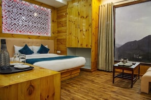 A bedroom with a large bed, wooden walls, a decorative panel, a window with curtains, and a view of mountains. - Jade Vine Resort (Shimla)