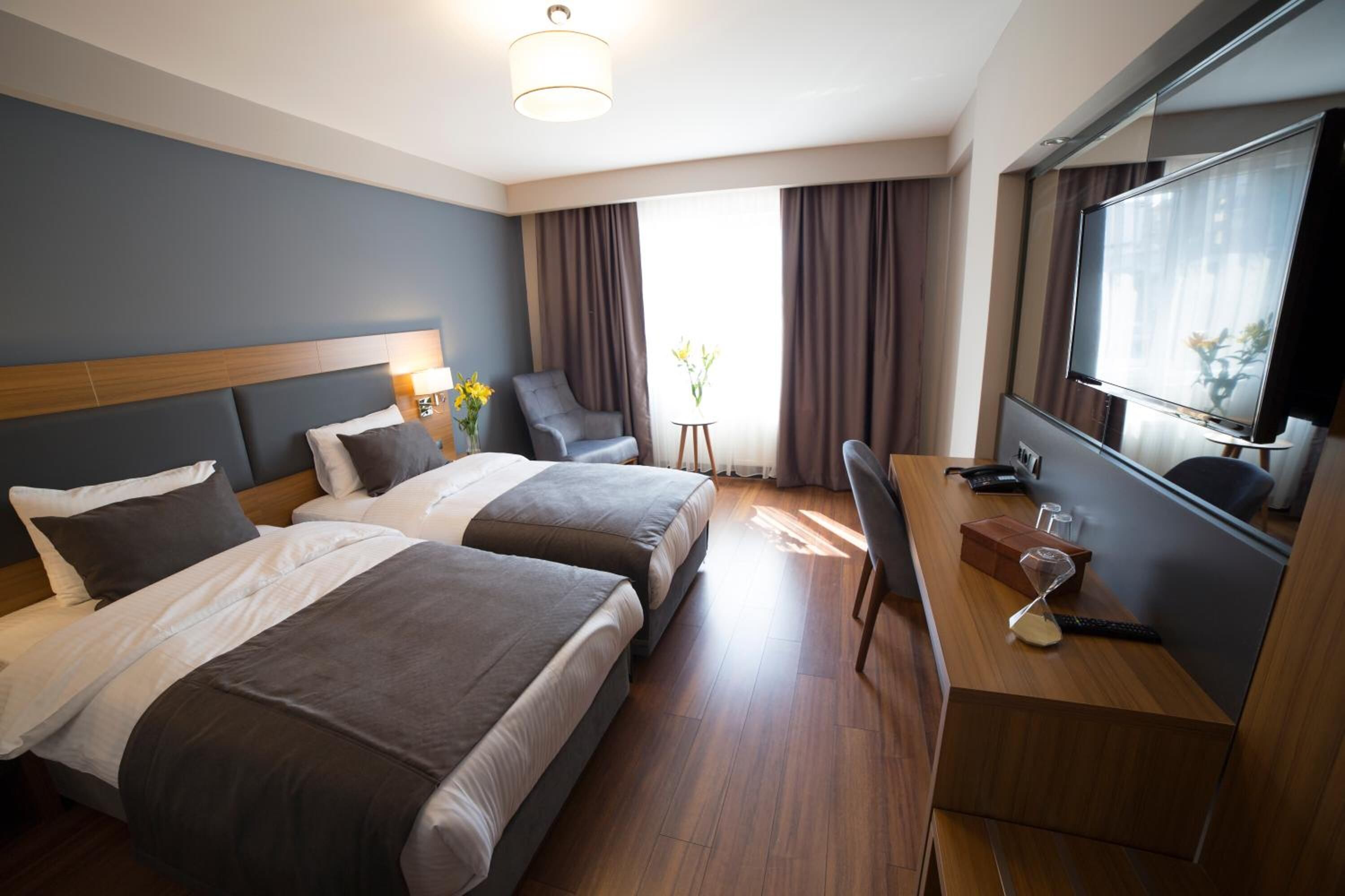 Habitación de hotel con dos camas, un escritorio, una silla, un televisor y una ventana con cortinas.