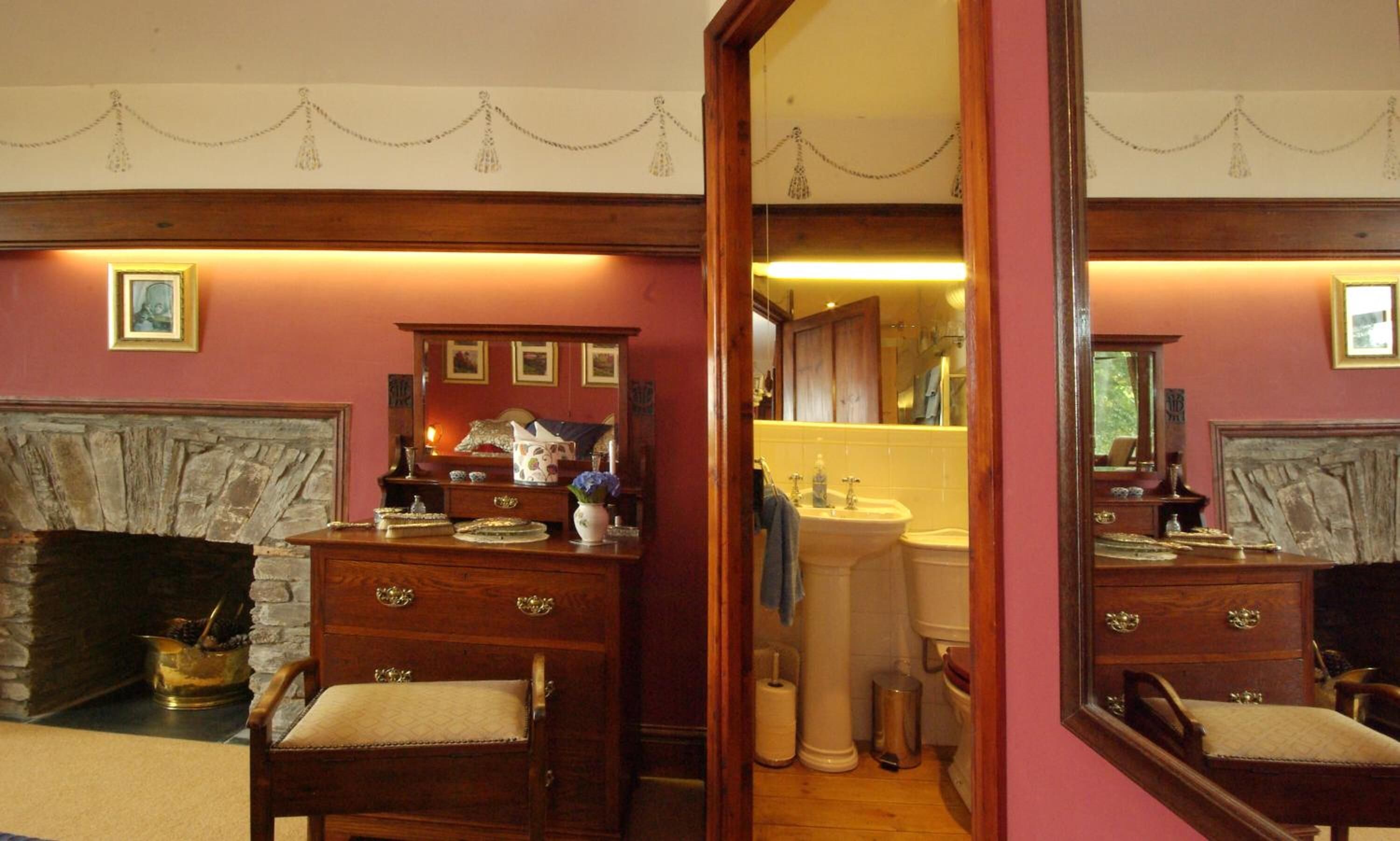 A room with a fireplace, wooden furniture, and a mirror reflecting the bathroom.