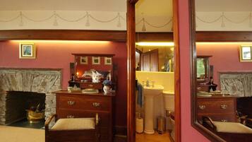 A room with a fireplace, wooden furniture, and a mirror reflecting the bathroom.