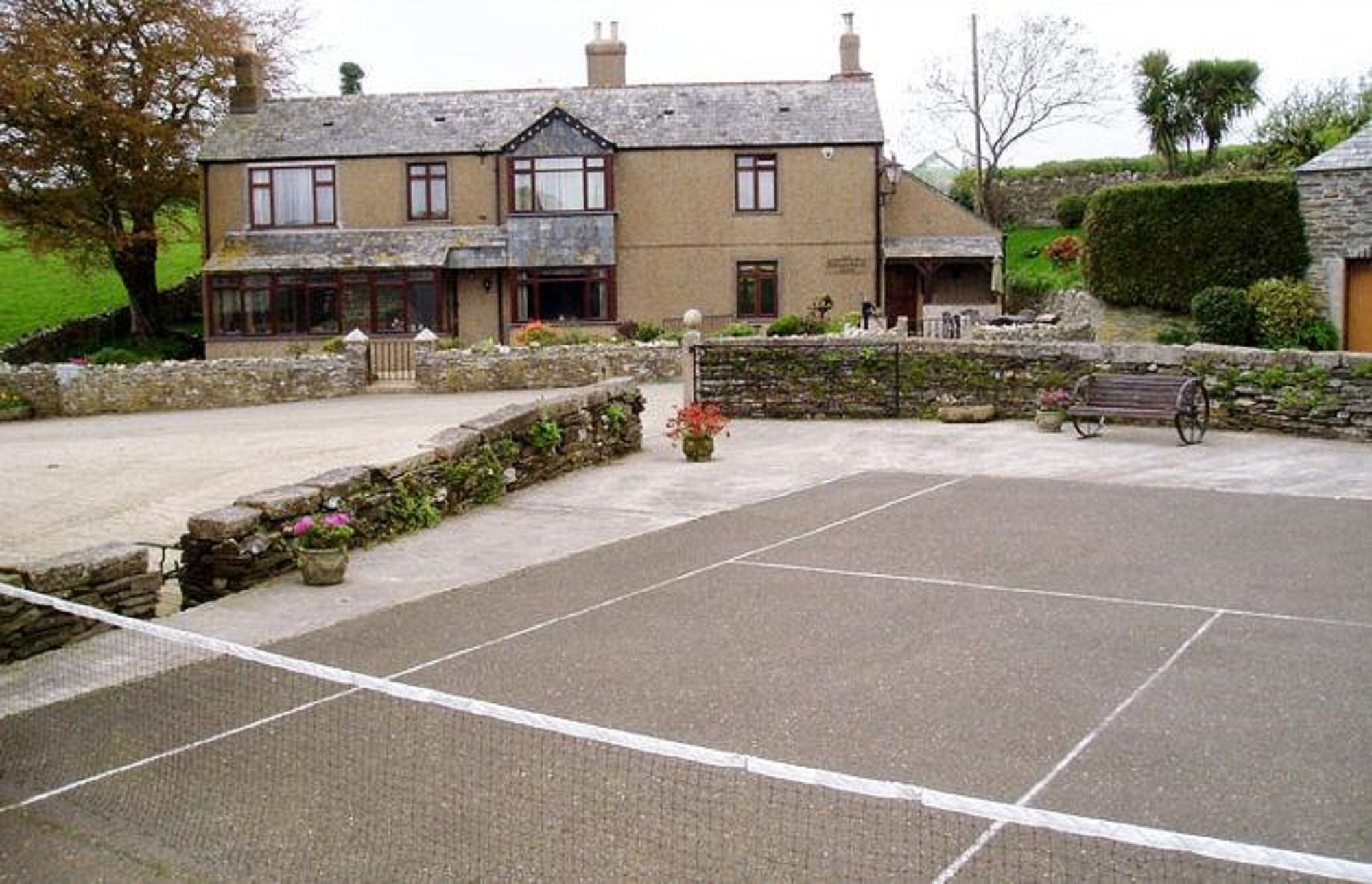 A courtyard with a tennis court, stone walls, and a building with multiple windows.
