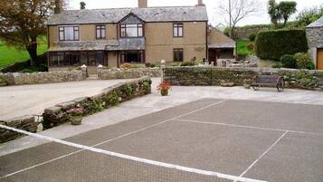 A courtyard with a tennis court, stone walls, and a building with multiple windows.