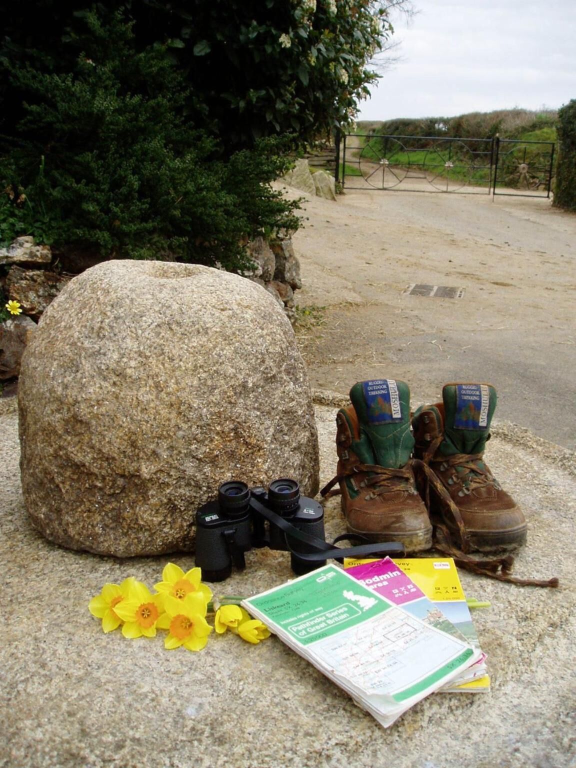 Un gros rocher, une paire de chaussures de randonnée, des jumelles et une carte posés sur une surface rocheuse.