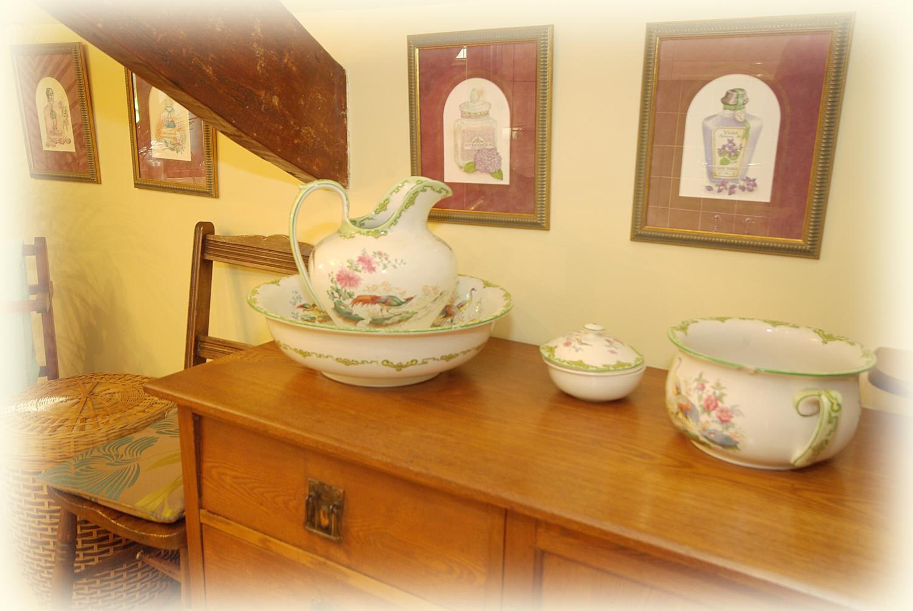 Una mesa de madera con una jarrón, un cuenco y una taza, junto con fotos enmarcadas en la pared.