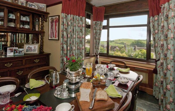 A dining room with a table set for breakfast, featuring a view of the countryside through a large window. - Tregondale Manor Farm (Liskeard)