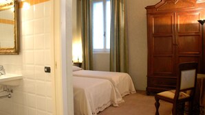 Une chambre avec deux lits, une armoire en bois, une chaise et une fenêtre avec des rideaux.