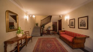 Un hall d’entrée spacieux, agrémenté d’une console en bois, d’un canapé rouge, d’un tapis à motifs, d’un escalier et d’un éclairage mural.
