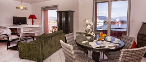 A living room with a sofa, dining table, chairs, a TV, and a view of a lake with mountains.