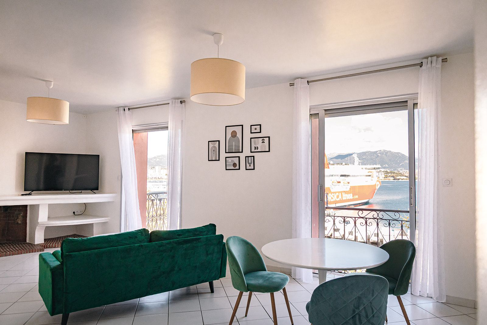 Un salon moderne avec un canapé vert, un téléviseur à écran plat, une table à manger avec des chaises et de grandes fenêtres donnant sur la mer.