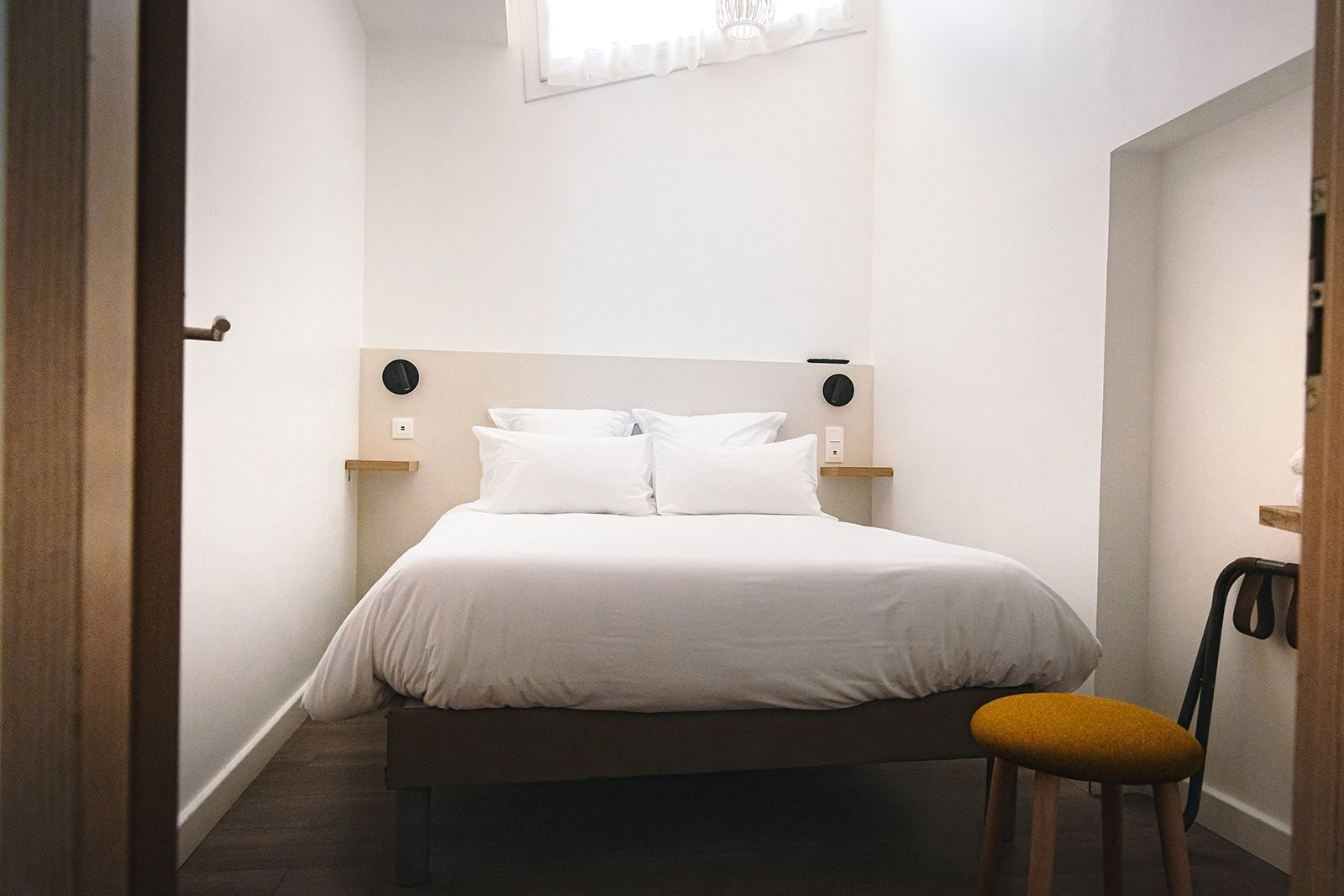 Un dormitorio con cama, mesita de noche, una silla y una ventana.